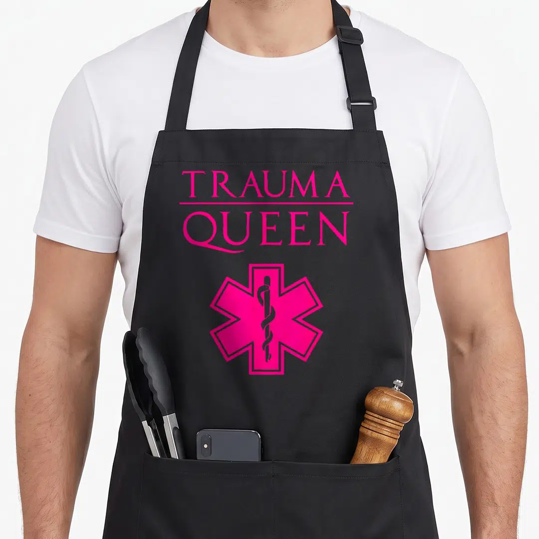 Paramedic queen apron - Pink stacked text reading TRAUMA QUEEN above a Star of Life symbol — shown on a black cotton canvas apron against a white background