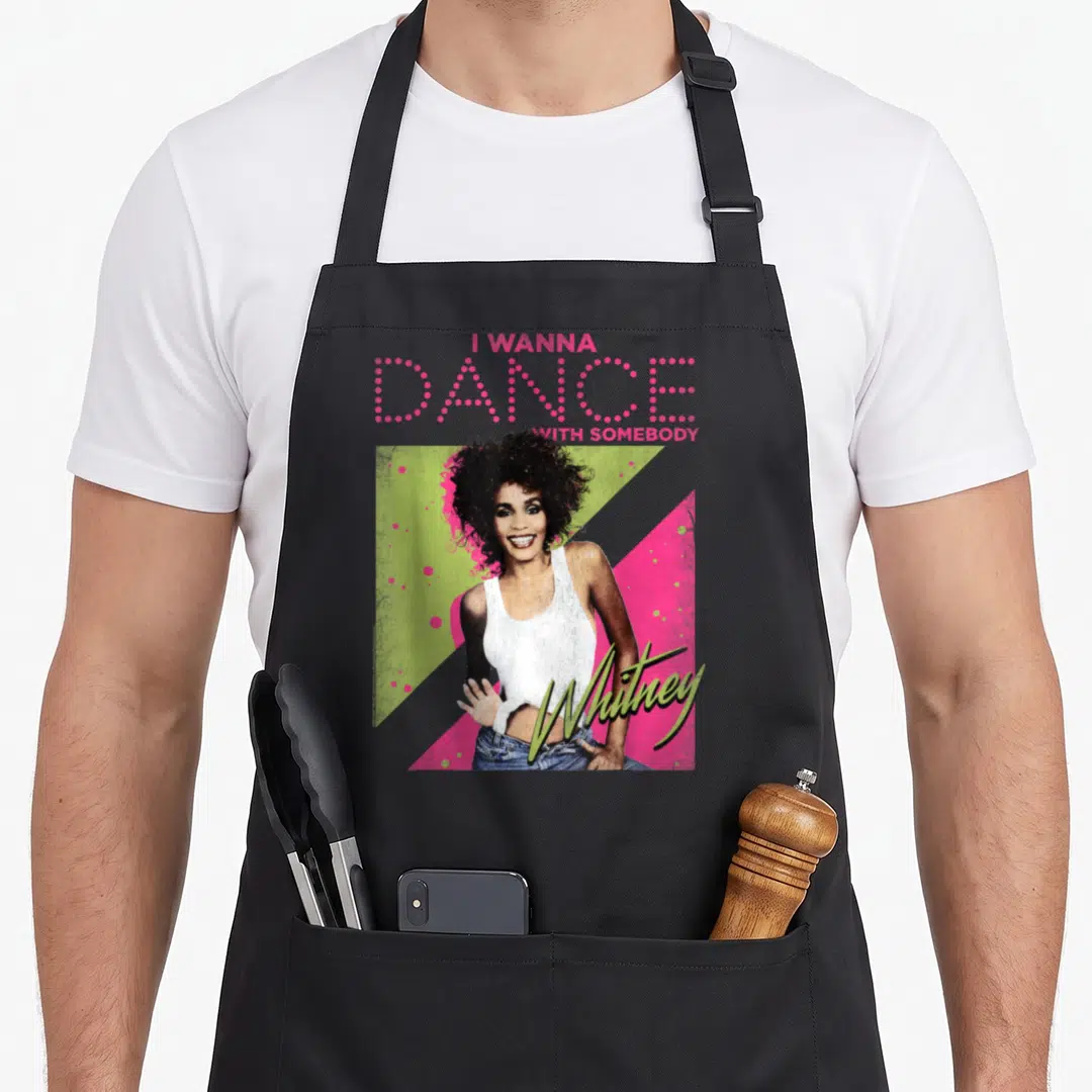 Dance houston problem apron - Whitney Houston photo with pink I WANNA DANCE WITH SOMEBODY text and green Whitney script — shown on a black cotton canvas apron against a white background