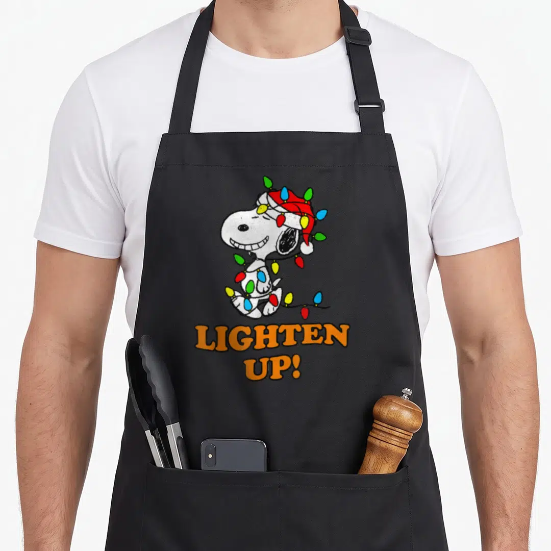 Lighten christmas apron - Snoopy in Santa hat wrapped in red, blue, green, yellow, and orange Christmas lights — shown on a black cotton canvas apron against a white background