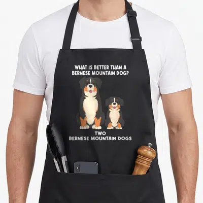 Better bernese dog apron - Cartoon of two Bernese Mountain Dogs sitting side by side with a pun question above — shown on a black cotton canvas apron against a white background