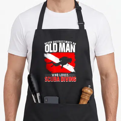 Underestimate diving apron - Diver silhouette on red white diagonal flag with distressed text NEVER UNDERESTIMATE — shown on a black cotton canvas apron against a white background