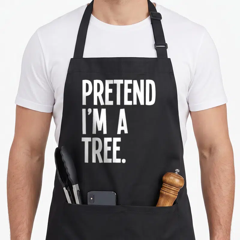 Pretend tree halloween apron - White stacked text reading PRETEND I'M A TREE on grey background — shown on a black cotton canvas apron against a white background