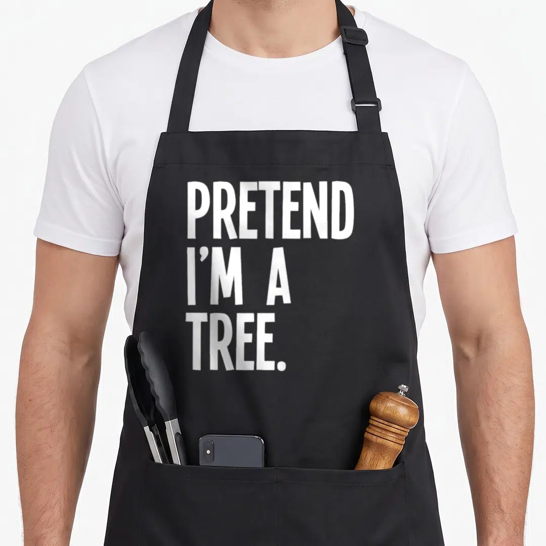Pretend tree halloween apron - White stacked text reading PRETEND I'M A TREE on grey background — shown on a black cotton canvas apron against a white background