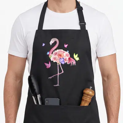 Nature pink flamingo apron - Watercolor pink flamingo with rose cluster midsection and scattered blue, yellow — shown on a black cotton canvas apron against a white background