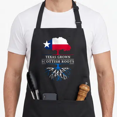 Scottish texas apron - Tree with Texas flag canopy and Scottish flag roots split by text TEXAS GROWN WITH SCOTTISH ROOTS — shown on a black cotton canvas apron against a white background