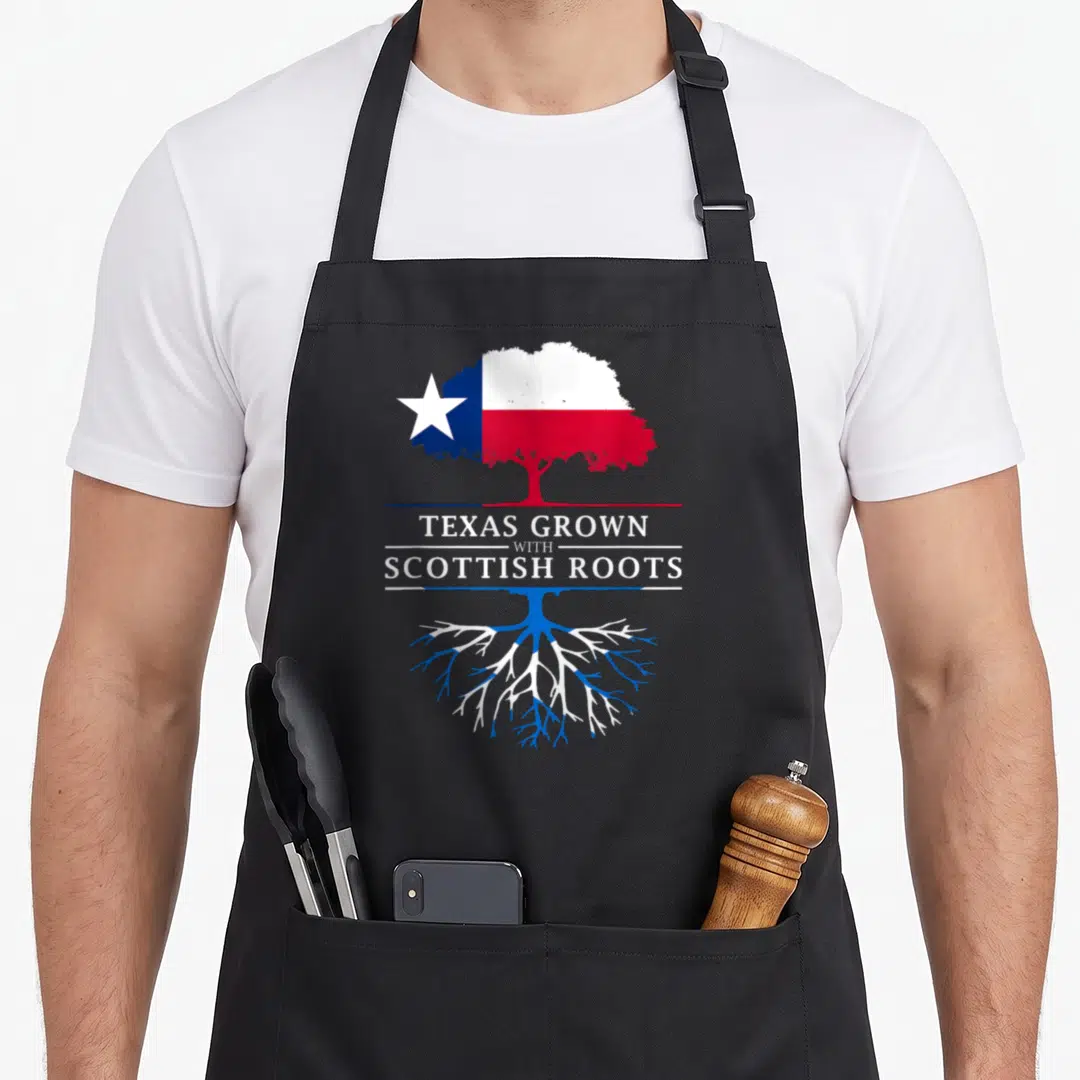 Scottish texas apron - Tree with Texas flag canopy and Scottish flag roots split by text TEXAS GROWN WITH SCOTTISH ROOTS — shown on a black cotton canvas apron against a white background