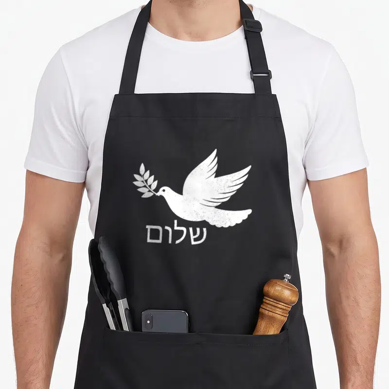 Shalom jewish aprons - White distressed dove holding olive branch above Hebrew text shalom — shown on a black cotton canvas apron against a white background