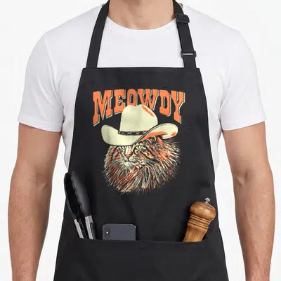 Timber southern aprons - Retro orange and cream cat wearing cowboy hat with MEOWDY text — shown on a black cotton canvas apron against a white background