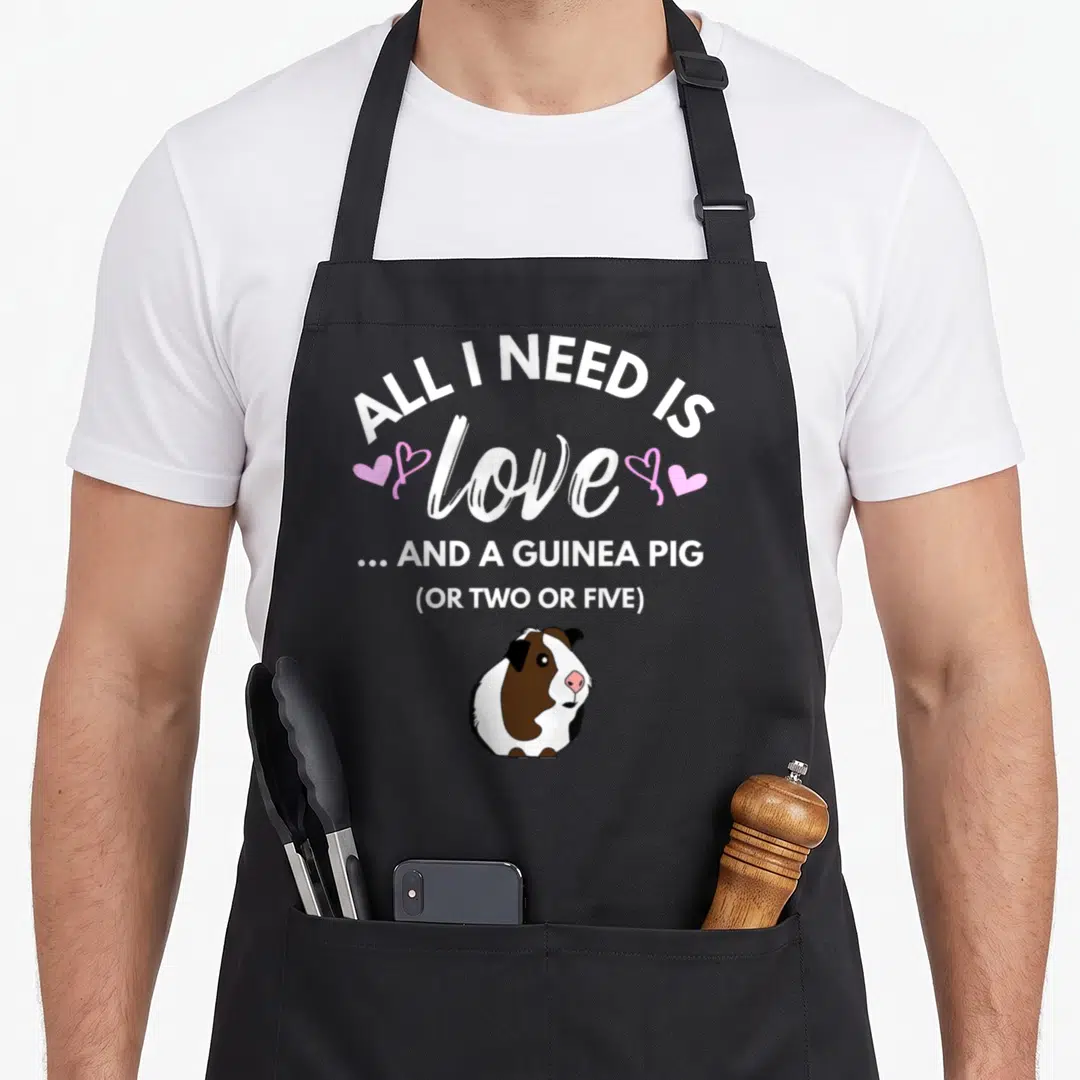 Funny pig i love my guinea apron - Stacked text reading All I Need Is Love And A Guinea Pig Or Two Or Five above — shown on a black cotton canvas apron against a white background