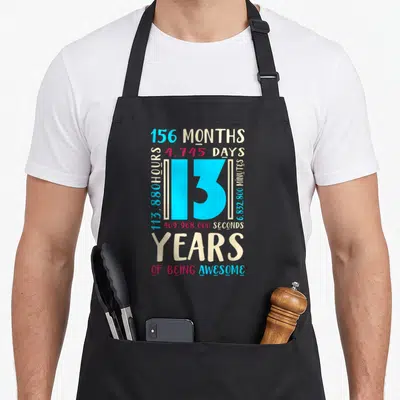 Age birthday apron - 13 years of being awesome time conversion typography in blue red beige — shown on a black cotton canvas apron against a white background
