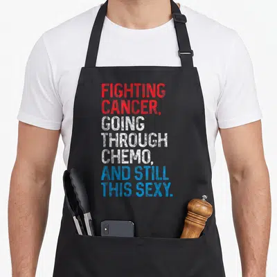 Cancer patient apron - Stacked red white and blue text reading Fighting Cancer Going Through Chemo And Still This Sexy — shown on a black cotton canvas apron against a white background