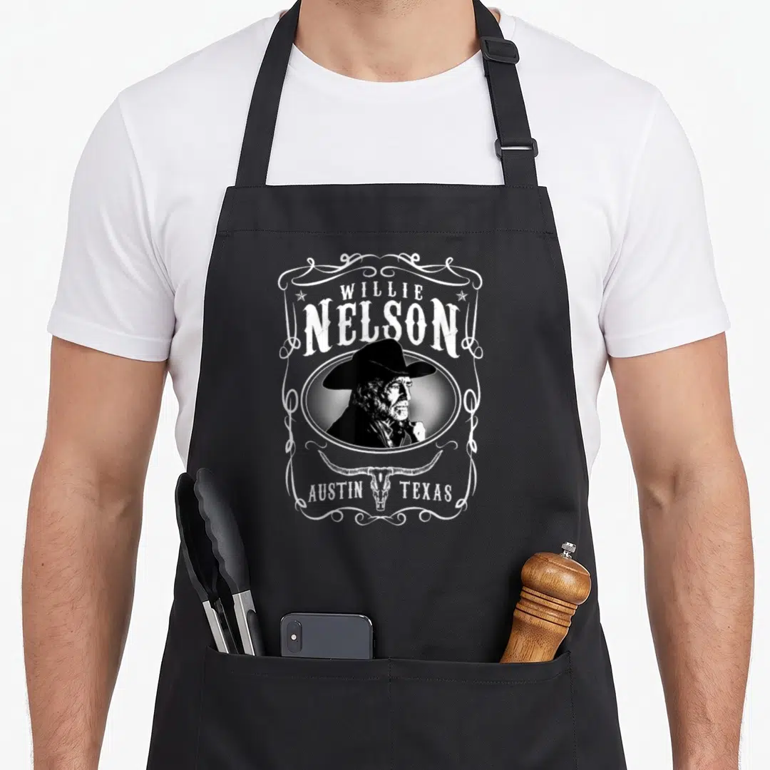 Willie austin apron - Willie Nelson portrait in oval above bull skull with Austin Texas text in white frame — shown on a black cotton canvas apron against a white background