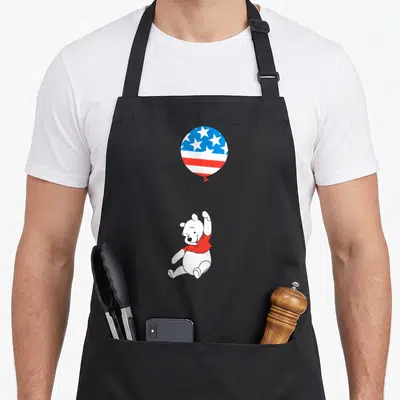 Americana balloon apron - Cartoon white bear in red shirt floating holding a patriotic star and stripe balloon — shown on a black cotton canvas apron against a white background