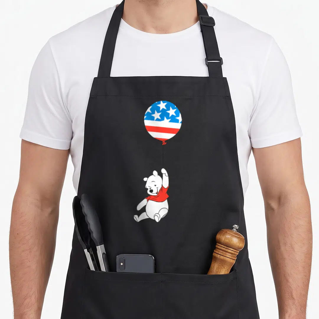 Americana balloon apron - Cartoon white bear in red shirt floating holding a patriotic star and stripe balloon — shown on a black cotton canvas apron against a white background