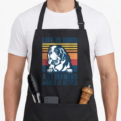 Saint dog apron - Retro St. Bernard head on striped sunset background with Life Is Good text — shown on a black cotton canvas apron against a white background