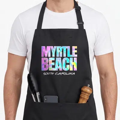 Myrtle tie-dye apron - Stacked Myrtle Beach South Carolina text in pink blue yellow tie dye font — shown on a black cotton canvas apron against a white background