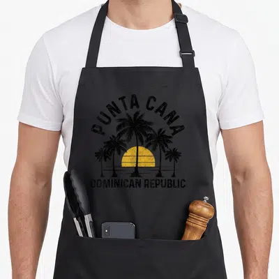 Punta dominican boy apron - Retro black palm trees and yellow sun with PUNTA CANA DOMINICAN REPUBLIC text — shown on a black cotton canvas apron against a white background