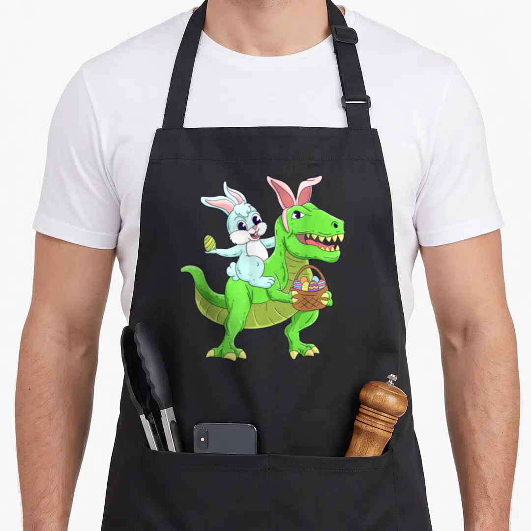 Riding easter bunny aprons - Light blue rabbit riding green dinosaur holding basket of colorful eggs — shown on a black cotton canvas apron against a white background