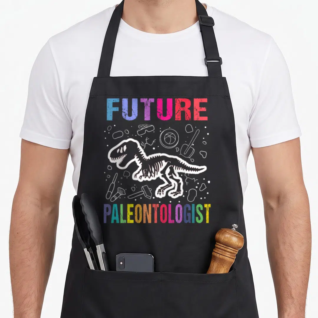 Future paleontologist dinosaur apron - Retro dinosaur skeleton with FUTURE PALEONTOLOGIST text and white tool outlines — shown on a black cotton canvas apron against a white background