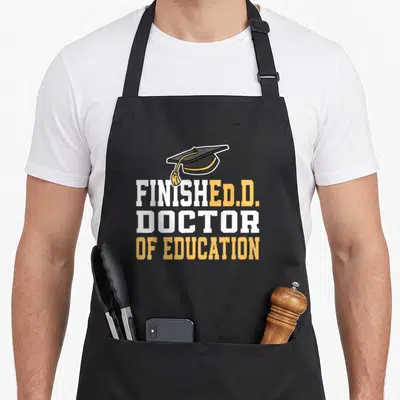 Finished education apron - Graduation cap above stacked white and yellow text reading FINISHED Ed.D. DOCTOR OF EDUCATION — shown on a black cotton canvas apron against a white background