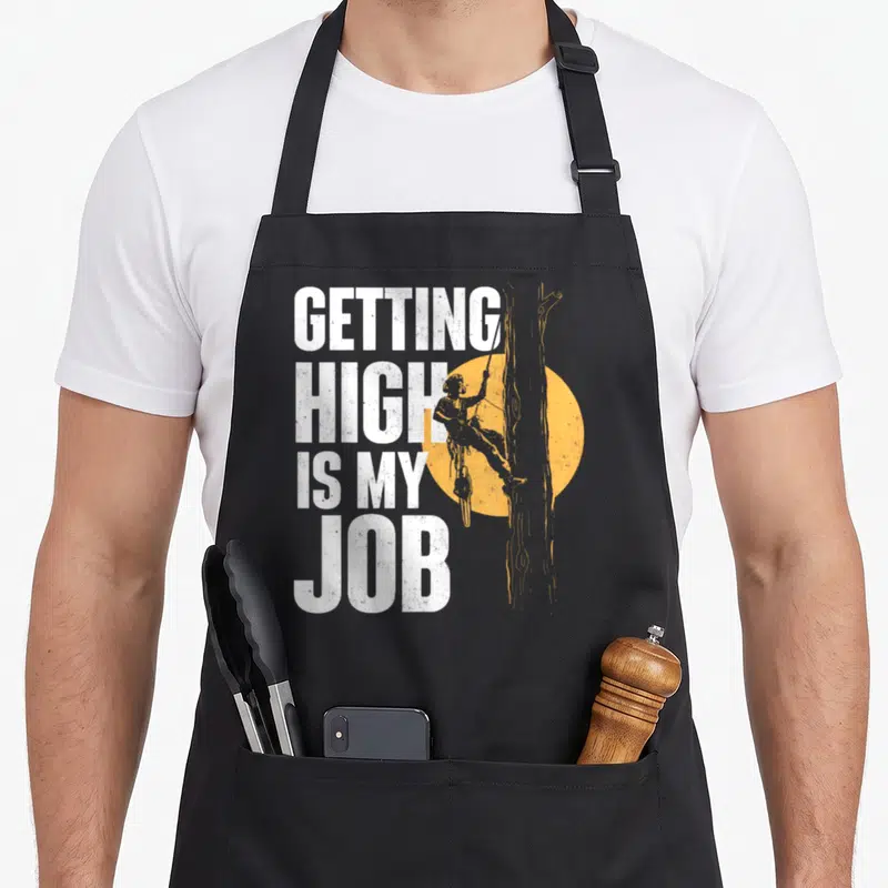Getting surgeon apron - White stacked text GETTING HIGH IS MY JOB next to orange arborist climbing tree silhouette — shown on a black cotton canvas apron against a white background