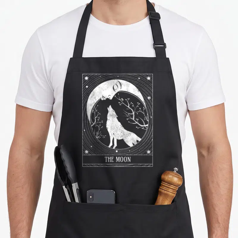 Crescent distressed apron - White line art wolf under moon with branches and stars in rectangular border with text — shown on a black cotton canvas apron against a white background