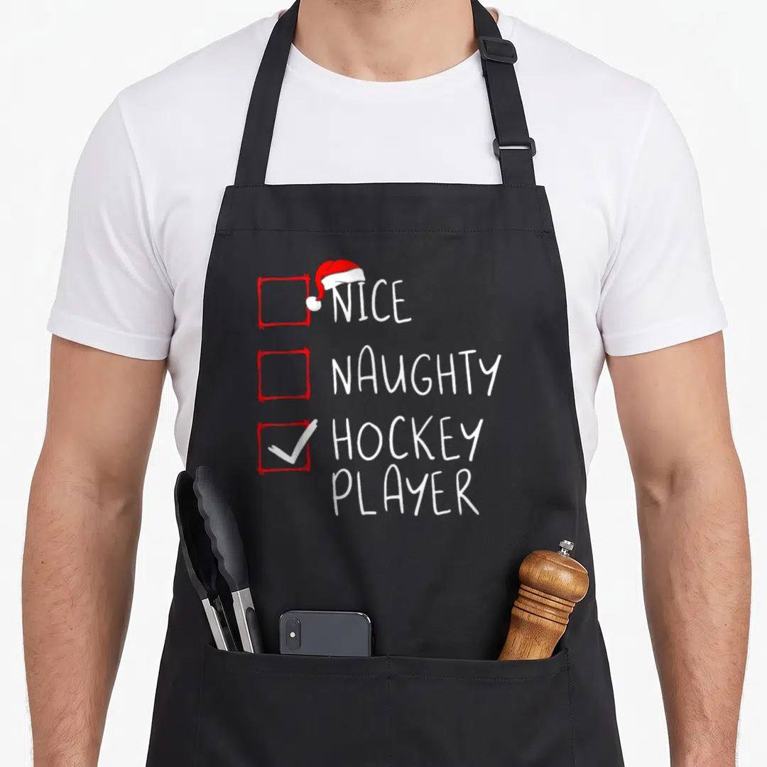 Hockey santa claus apron - Red and white checklist with Santa hat checking off hockey player instead of nice or naughty — shown on a black cotton canvas apron against a white background