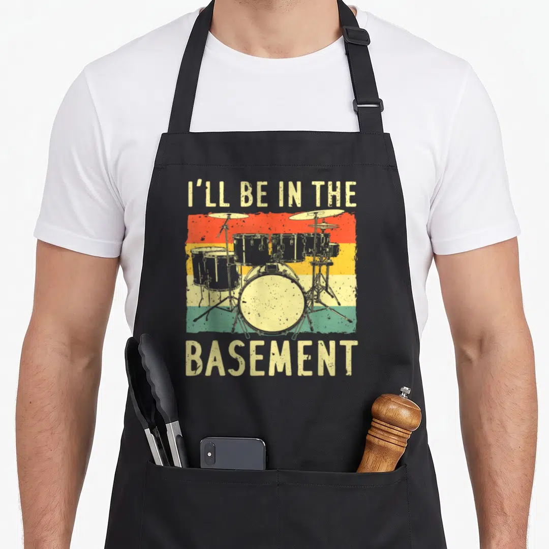 Drumming drum set apron - Retro drum kit on red yellow green stripes with I'll be in the basement text — shown on a black cotton canvas apron against a white background