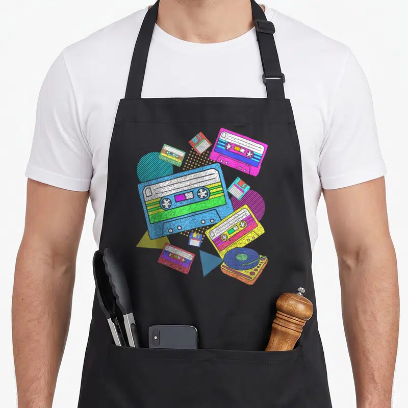 Eighty theme aprons - Retro collage of blue pink yellow green cassettes and geometric shapes — shown on a black cotton canvas apron against a white background
