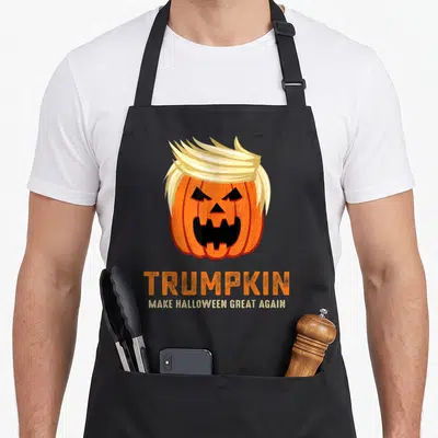Funny trumpkin halloween apron - Orange pumpkin with blonde hair and TRUMPKIN text — shown on a black cotton canvas apron against a white background