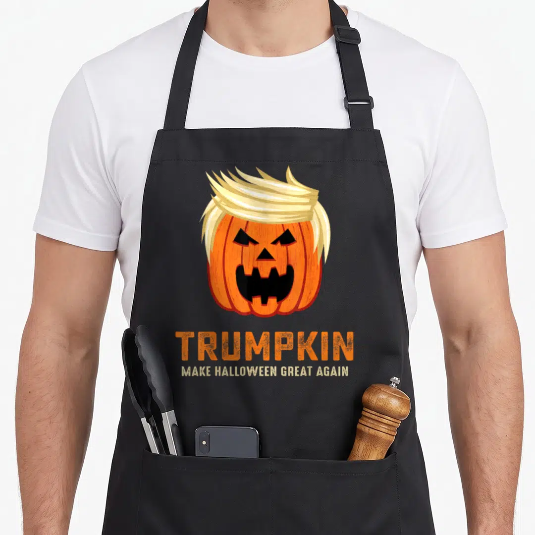 Funny trumpkin halloween apron - Orange pumpkin with blonde hair and TRUMPKIN text — shown on a black cotton canvas apron against a white background