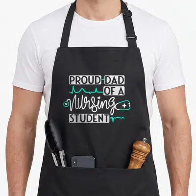 Student nurses apron - PROUD DAD OF A Nursing STUDENT text with teal stethoscope and heartbeat line — shown on a black cotton canvas apron against a white background