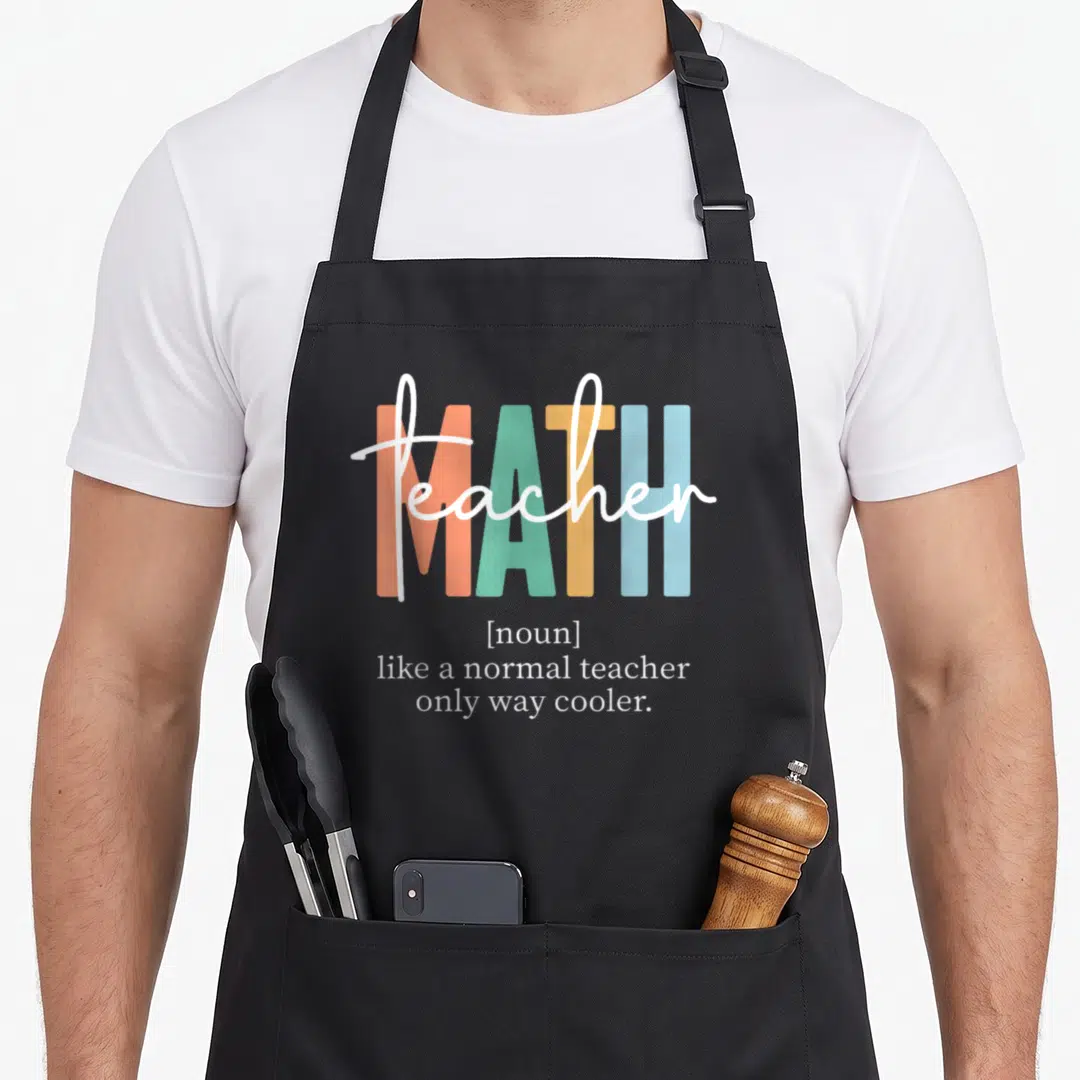 Math definition teacher apron - MATH in orange green yellow blue blocks with teacher script and white definition text — shown on a black cotton canvas apron against a white background