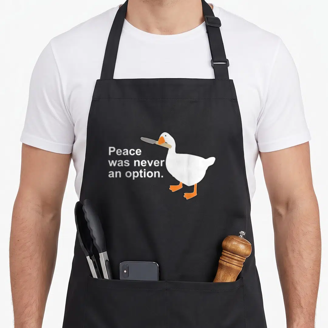 Peace goose apron - White cartoon goose holding a knife next to text reading Peace was never an option — shown on a black cotton canvas apron against a white background