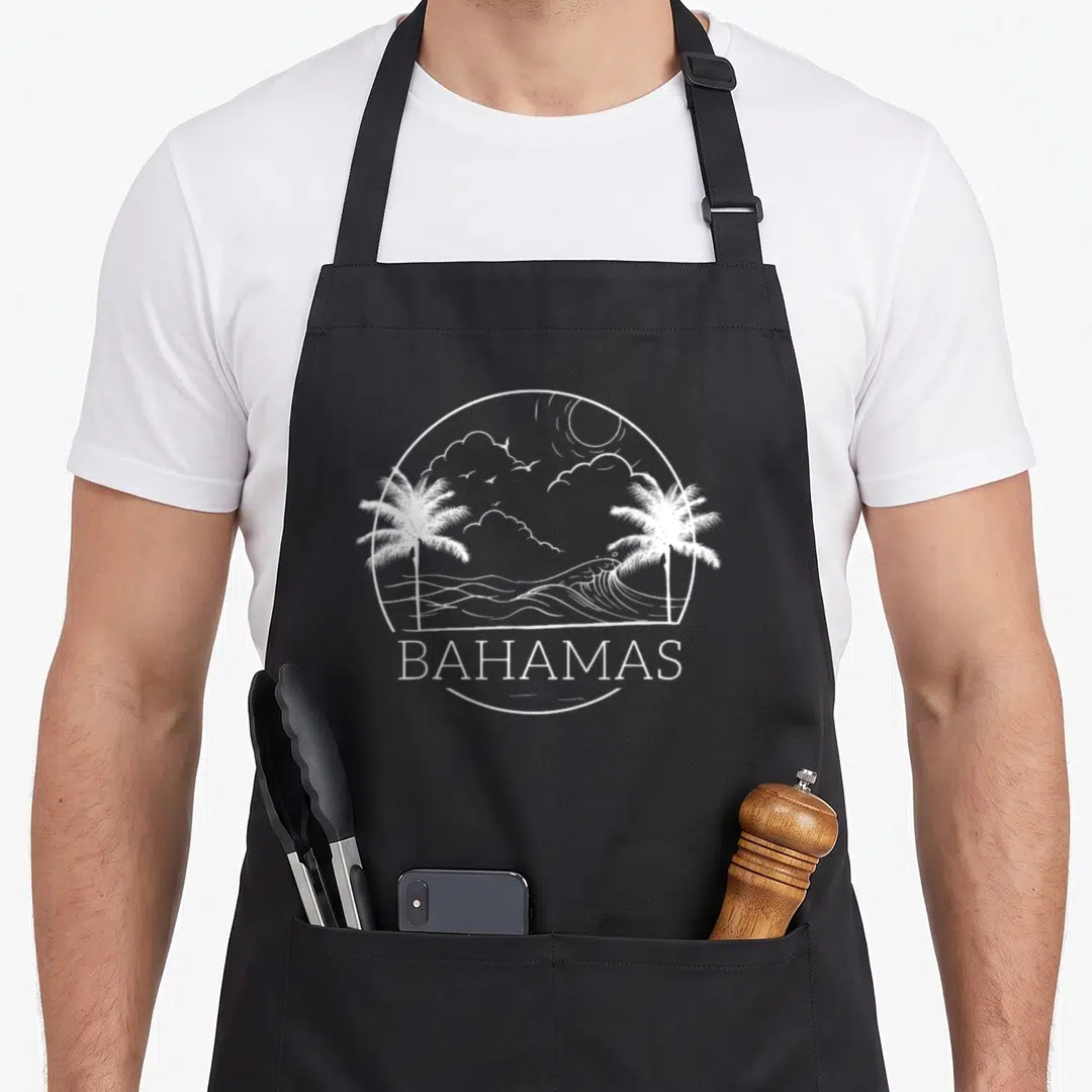 Proud bahamas flag bahamian apron - White circular line art of palm trees and ocean waves above the word BAHAMAS — shown on a black cotton canvas apron against a white background