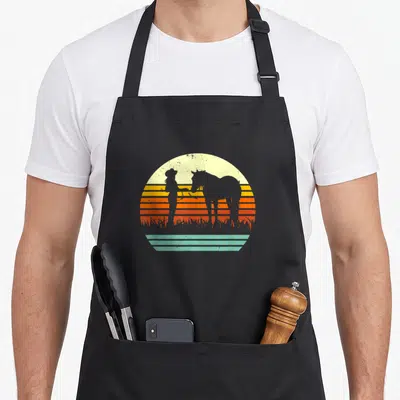 Cowgirl western apron - Retro sunset silhouette of cowgirl and horse in yellow orange red and teal stripes — shown on a black cotton canvas apron against a white background