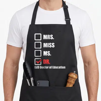 Graduation doctor apron - Checklist with MRS MISS MS DR checked in red and EdD Doctor of Education text below — shown on a black cotton canvas apron against a white background