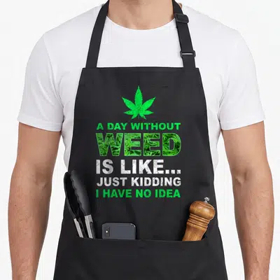 Weed pot apron - Green cannabis leaf above stacked text WEED filled with plant photo and distressed white lettering — shown on a black cotton canvas apron against a white background