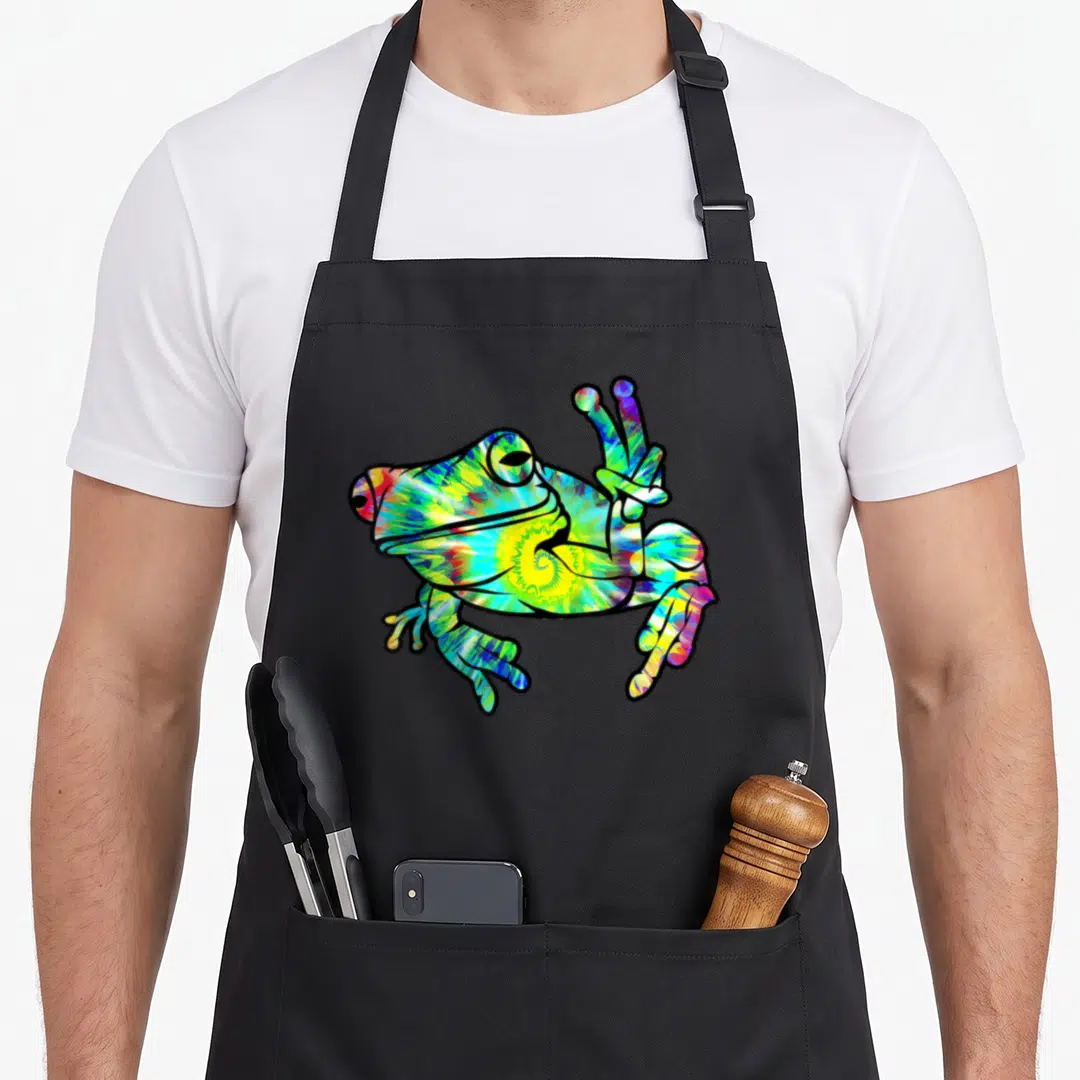 Frog tie dye apron - Multicolored frog in tie-dye pattern holding up a peace sign with two fingers — shown on a black cotton canvas apron against a white background
