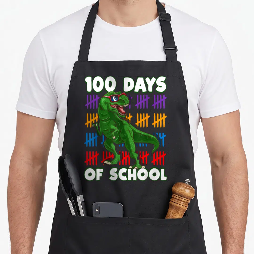 School worlds greatest apron - Green T-Rex sunglasses 100 Days of School purple orange blue red tally marks — shown on a black cotton canvas apron against a white background