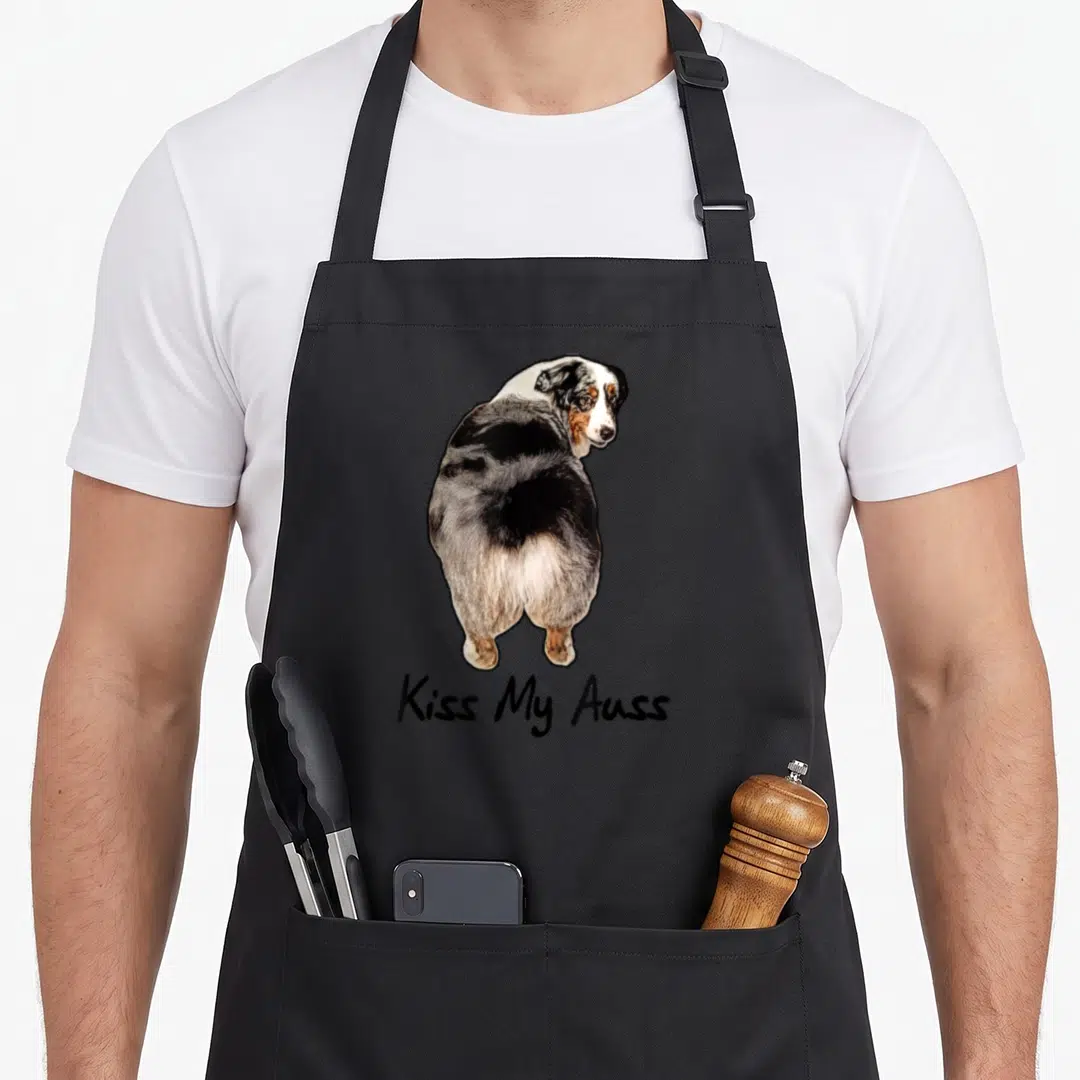 Miniature australian aprons - Realistic black white brown dog facing back with text Kiss My Auss below — shown on a black cotton canvas apron against a white background