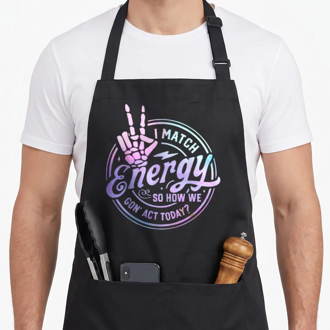 Match halloween apron - Holographic circle with skeleton hand peace sign and I Match Energy quote in pink and blue — shown on a black cotton canvas apron against a white background