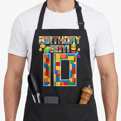 10th building aprons - BIRTHDAY BOY! and number 10 made of colorful toy blocks — shown on a black cotton canvas apron against a white background