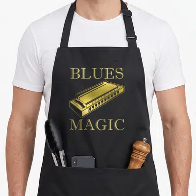 Blue french apron - Gold harmonica illustration with BLUES MAGIC text in minimalist style — shown on a black cotton canvas apron against a white background