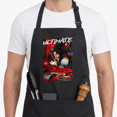 Shadow ultimate apron - Shadow the Hedgehog running with ULTIMATE and POWER text over red city lights — shown on a black cotton canvas apron against a white background