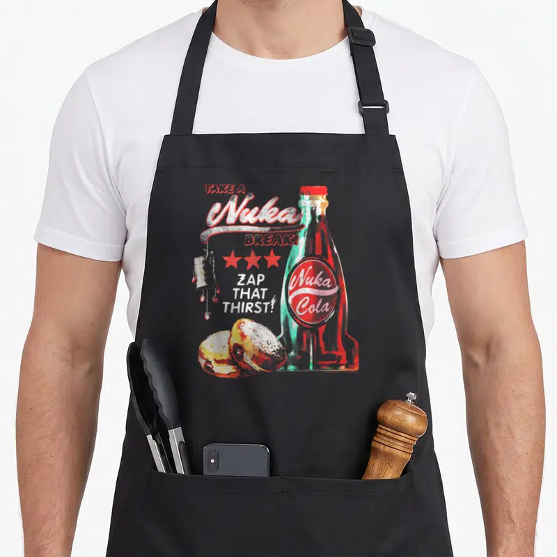 Nuka video game apron - Retro Nuka Cola bottle, three red stars, scattered text, and food items in red and teal — shown on a black cotton canvas apron against a white background