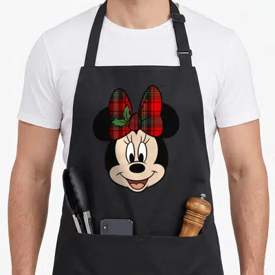 Bow christmas apron - Minnie Mouse head with red plaid bow and green holly leaves on black background — shown on a black cotton canvas apron against a white background