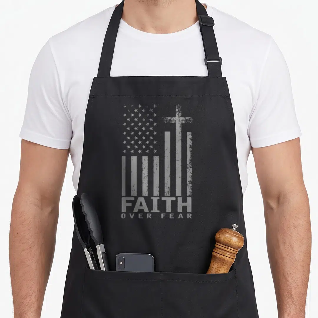 Flag pride apron - Grey distressed American flag with integrated cross and stacked FAITH OVER FEAR text — shown on a black cotton canvas apron against a white background