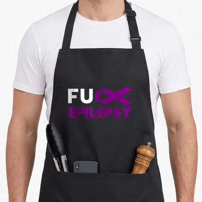 Epilepsy funk apron - FUC EPILEPSY text with purple ribbon replacing letter K on grey background — shown on a black cotton canvas apron against a white background