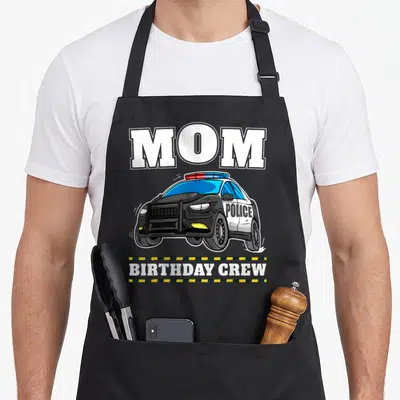 Police crew aprons - MOM BIRTHDAY CREW text surrounding a cartoon police car with yellow and black caution tape border — shown on a black cotton canvas apron against a white background